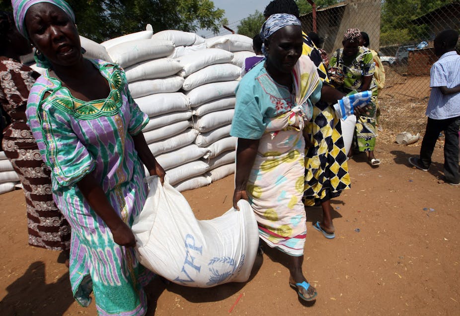 Women carrying sack of food marked with World Food Programme logo. 
