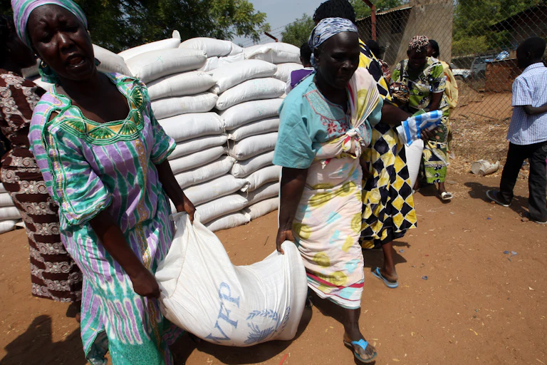 Women carrying sack of food marked with World Food Programme logo.