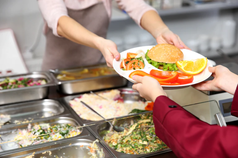 Hands passing a plate of food in a cafeteria.