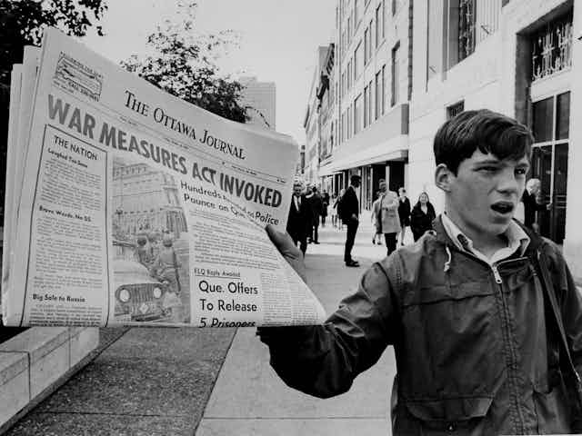 A boy holds up a newspaper with the banner headline War Measures Act invoked.