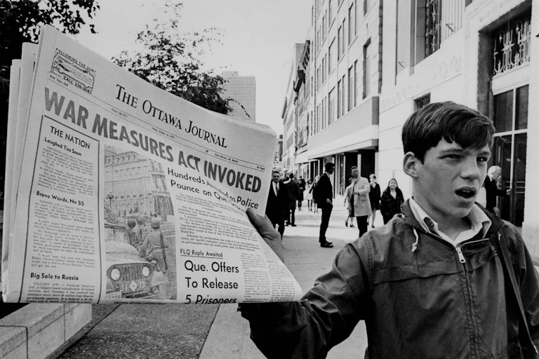 A boy holds up a newspaper with the banner headline War Measures Act invoked.