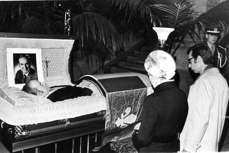 Pierre Laporte's open casket, with two people kneeling in front of it.