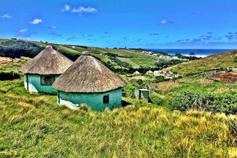 Xhosa huts on along South Africa's Wild Coast with the mountains and the ocean and a backdrop.