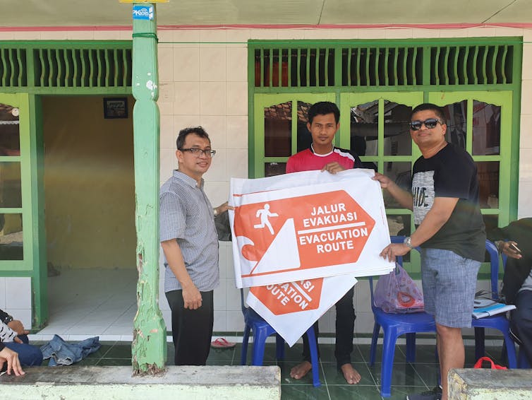 Three men hold up a tsunami evacuation route sign.