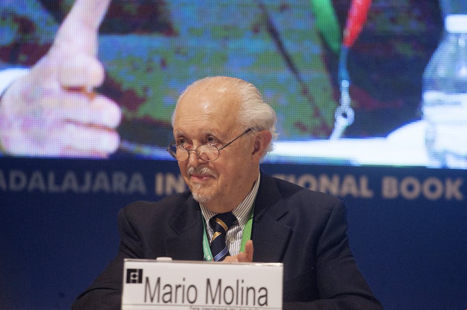 Molina, with glasses, white hair and a goatee, sits on a panel