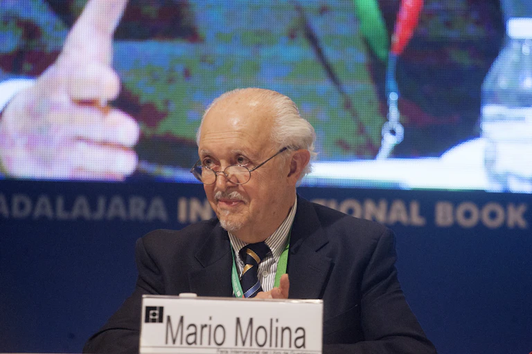 Molina, with glasses, white hair and a goatee, sits on a panel