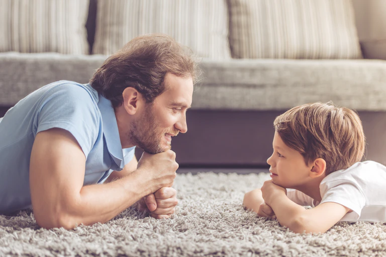 A father and son lying on the floor and chatting face to face.