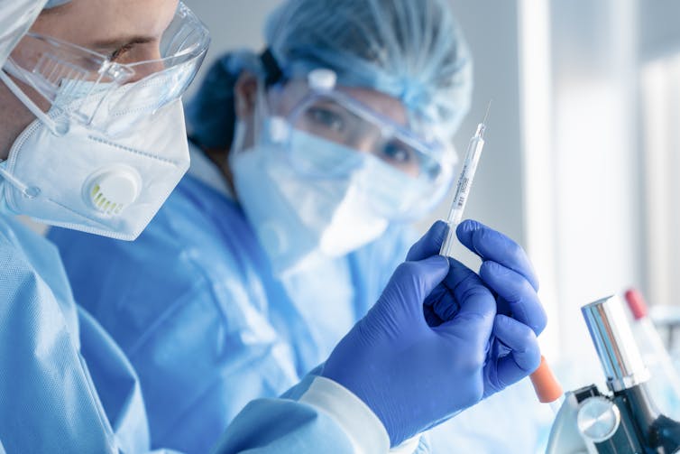 Two scientists in a lab look at a syringe.