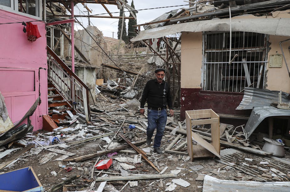 A man walks in between damaged houses.