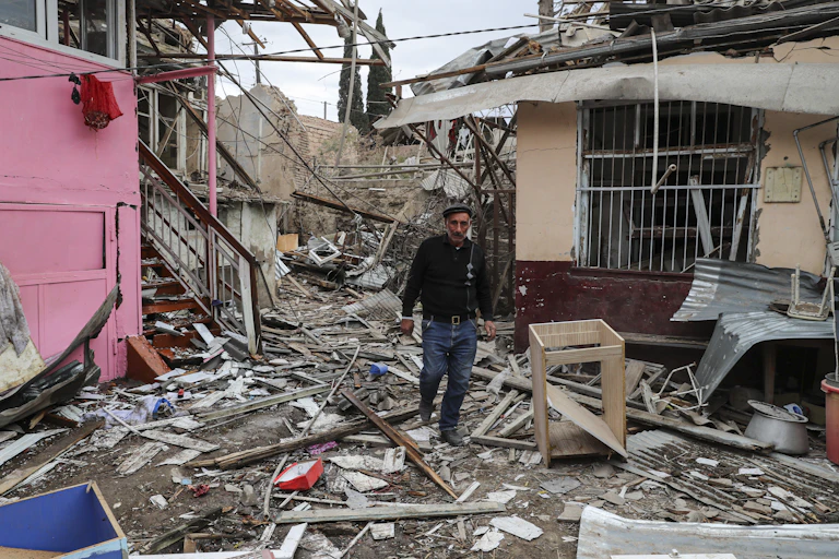 A man walks in between damaged houses.