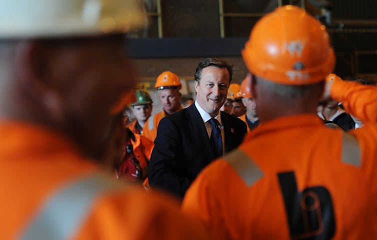 Prime Minister David Cameron meets workers in orange uniforms and hard hats in 2012.