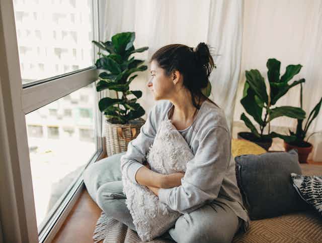 Sad woman looking out of window of apartment
