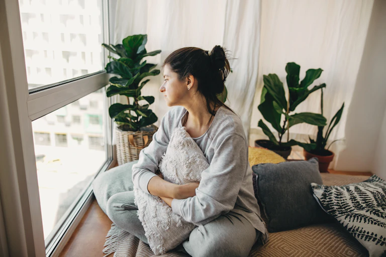 Sad woman looking out of window of apartment