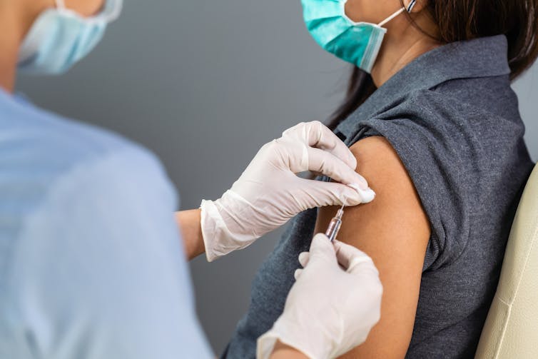 A woman weaing a mask receives a vaccine from an health worker