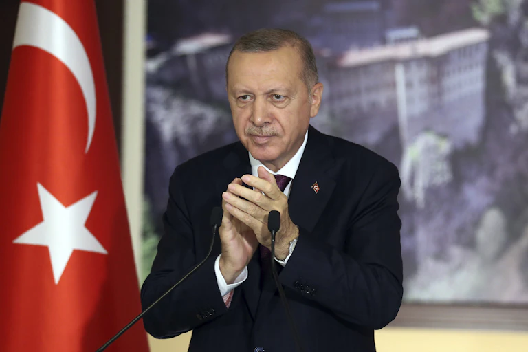 Turkey's Recep Tayyip Erdogan applauds as he stands behind a microphone and beside the Turkish flag.