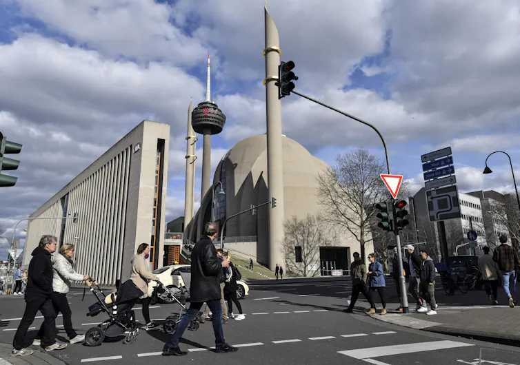 People cross a street at an intesection with a mosque in the background.