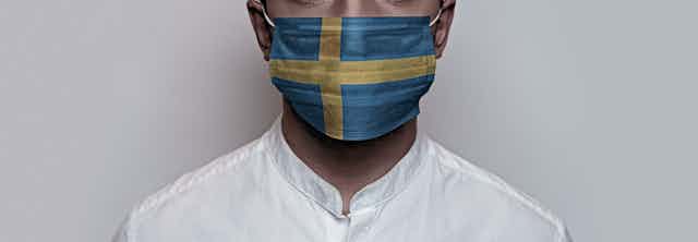 Un hombre con camisa blanca y mascarilla ilustrada con la bandera sueca