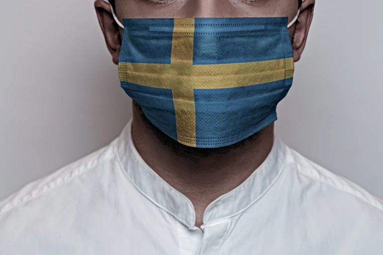 Un hombre con camisa blanca y mascarilla ilustrada con la bandera sueca