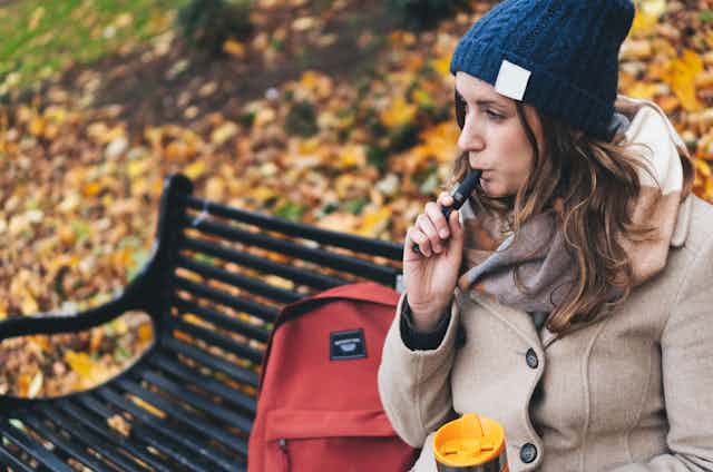 Woman sitting on park bench smoking an e-cigarette