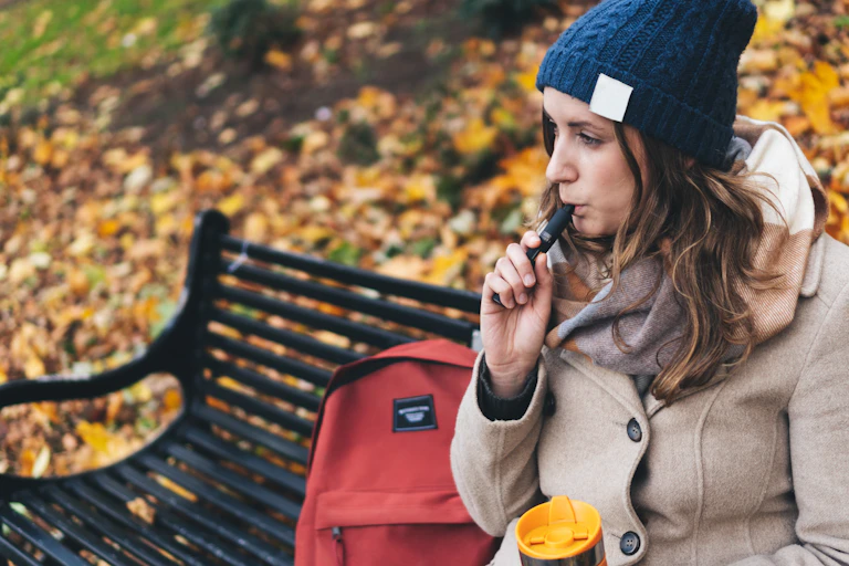 Woman sitting on park bench smoking an e-cigarette