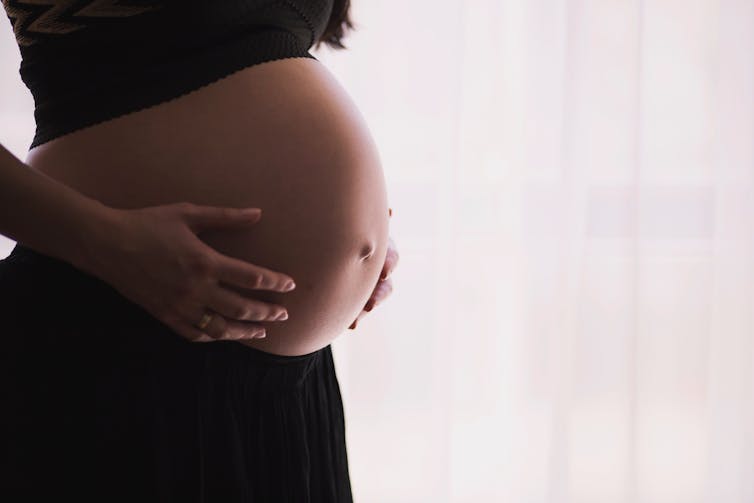 A woman holds her pregnant belly.