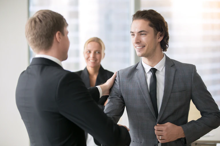 Two men in suits shaking hands with woman in background.
