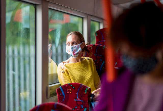 masked woman looks out bus window