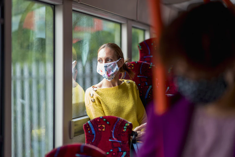 masked woman looks out bus window