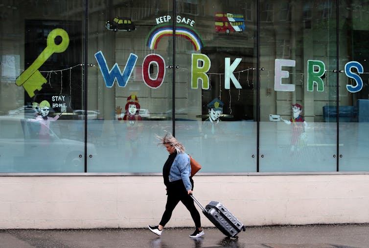 A woman wheels a suitcase past a window decorated with a key and the word 'workers'