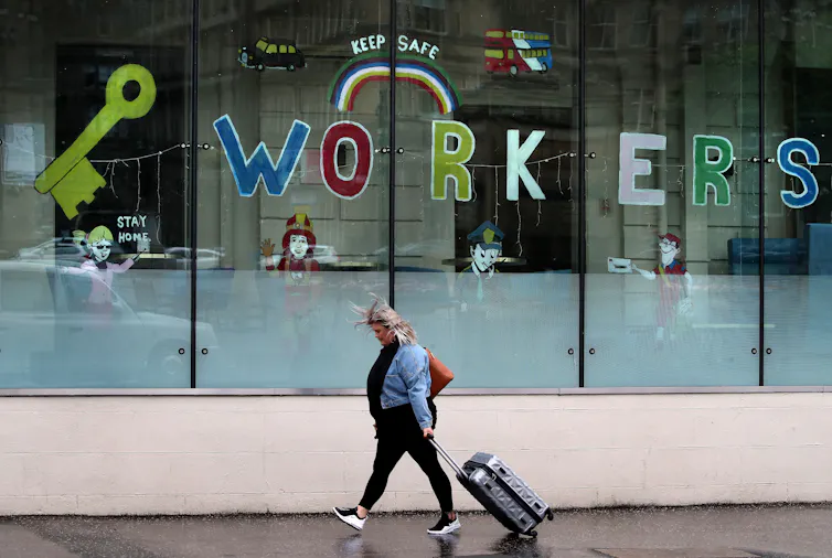 A woman wheels a suitcase past a window decorated with a key and the word 'workers'
