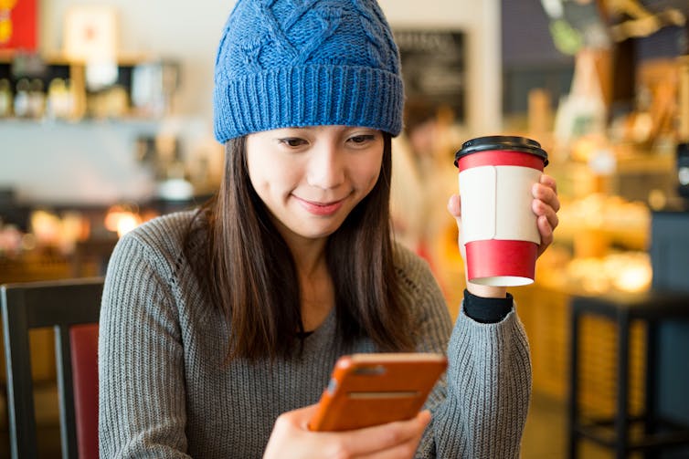 Woman holding phone and coffe cup sitting in a cafe.