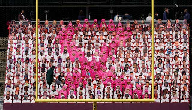 A large breast cancer pink ribbon made up of individual pink ribbon placards in the stadium seats at a football game.