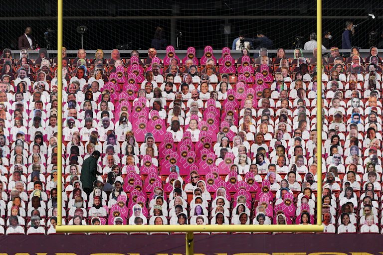 A large breast cancer pink ribbon made up of individual pink ribbon placards in the stadium seats at a football game.