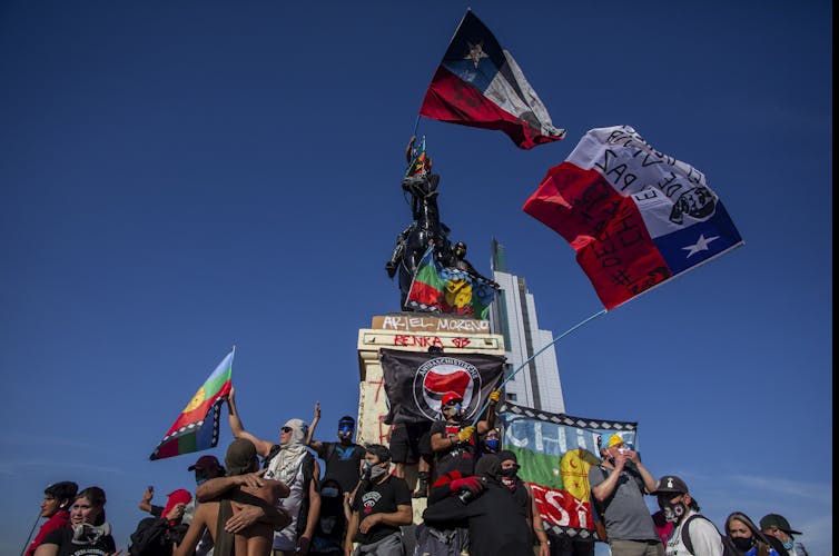 Chileans wave flags while standing on a graffiti-covered national monument.