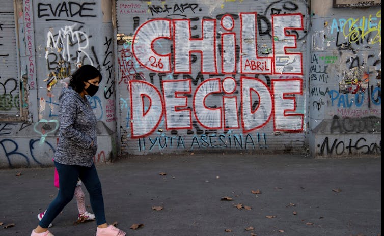 Una mujer con una mascarilla pasa junto a un graffiti que lee 'Chile Decide'