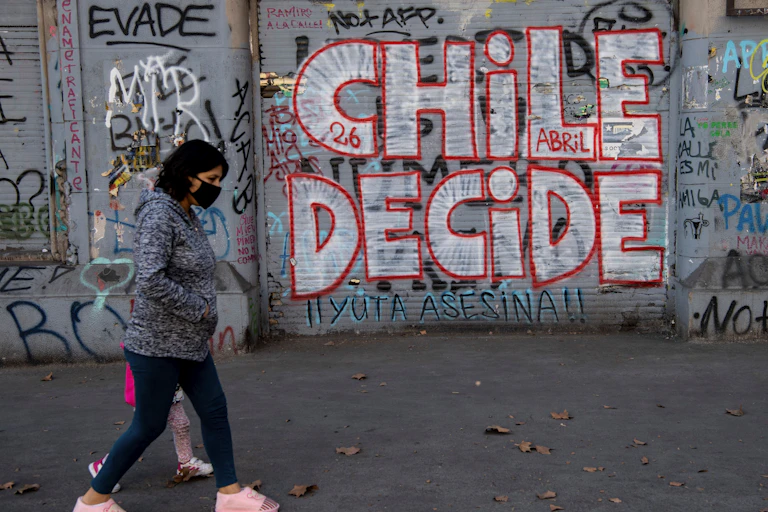 A woman in a face mask walks past a graffiti reading Chile Decides