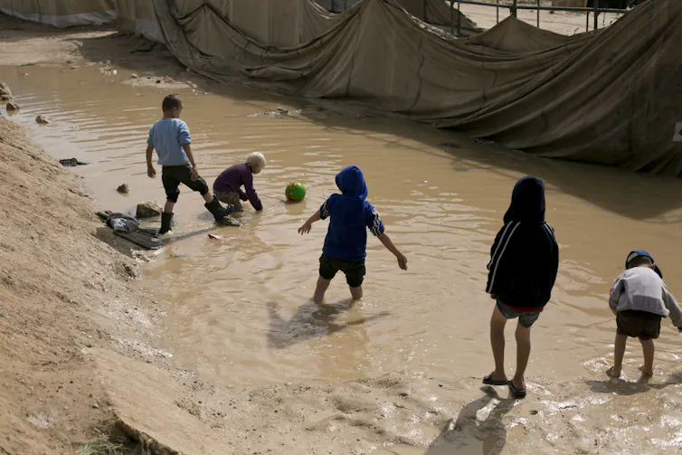 Five children playing in a large mud puddle