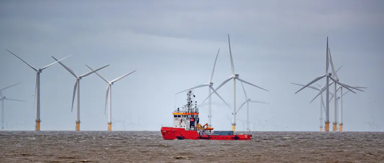 A red ship passes in front of wind turbines.