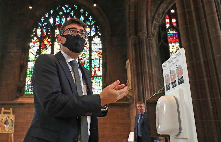 Andy Burnham santising his hands at a memorial service.