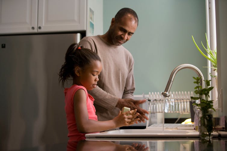 A man and his daughter wash dishes together.