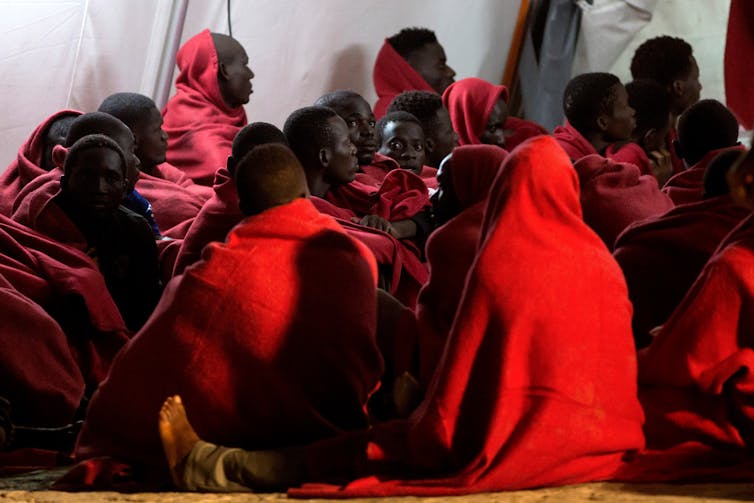 A group of people wearing red sit huddled on the floor.
