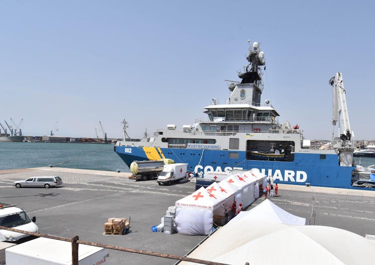 A coast guard ship in port next to red cross tents.
