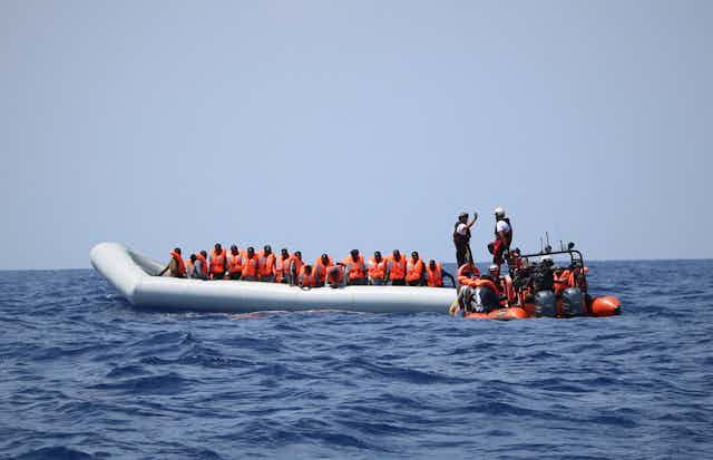 A group of migrants in orange life jackets in a rescue boat in the Mediterranean Sea.