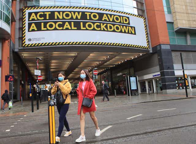 Shoppers walking in front of a sign warning about the potential for a local lockdown.