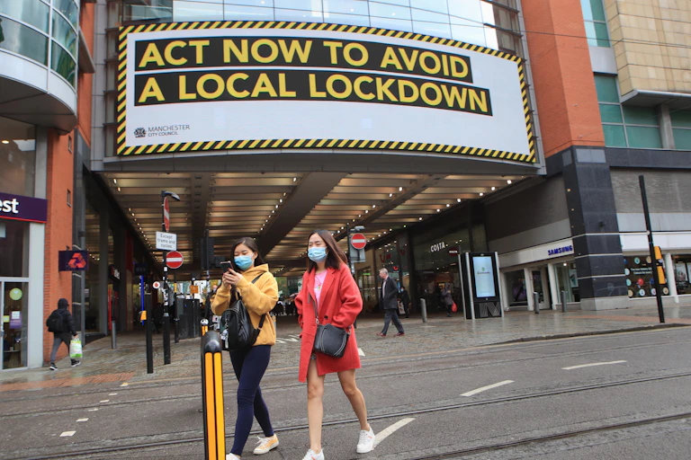 Shoppers walking in front of a sign warning about the potential for a local lockdown.
