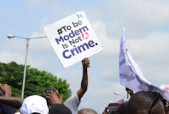 A man holds up a square white placard reading, '#To be Modern is Not A Crime'