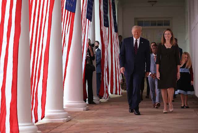 Trump and Barrett walk down a colonnade adorned with American flags