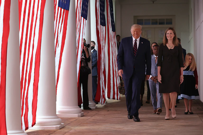 Trump and Barrett walk down a colonnade adorned with American flags