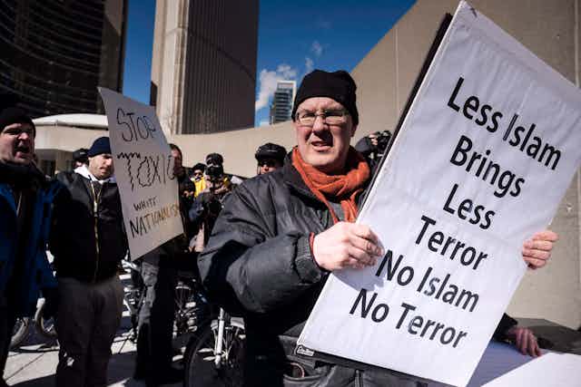 A white man holds a sign saying LESS ISLAM BRINGS LESS TERROR NO ISLAM NO TERROR