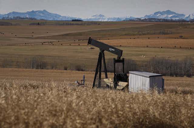 A pumpjack on a farmer's field with mountains in the background